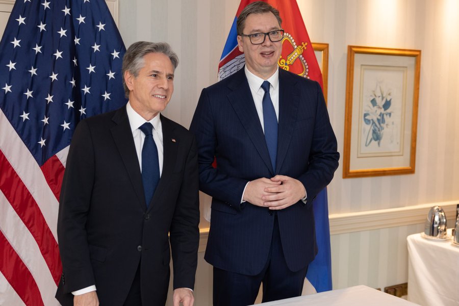 Secretary Blinken and Serbian President Vucic smile for a photo while standing in front of their country flags.    