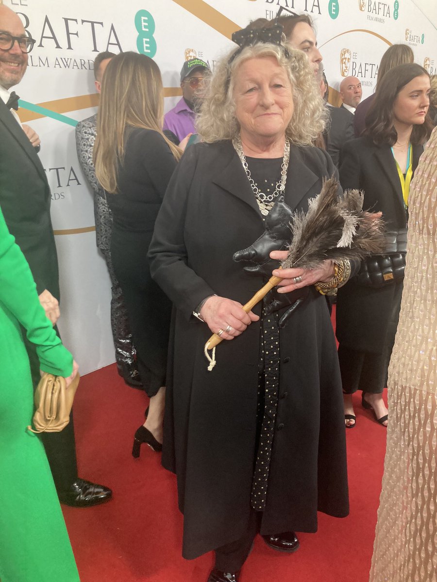 Costume Designer Jenny Beavan is having fun at The BAFTAs. In 2016 Stephen Fry joked she looked like a “bag lady”. This time she’s come as a cleaning lady, complete with duster. That is the occupation of Mrs Harris in Mrs Harris goes to Paris, the film she is nominated for.