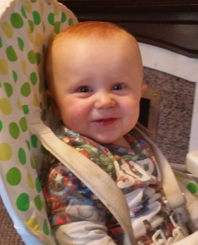 Cameron smiling to the camera in his high chair.