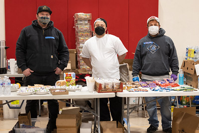 A picture of three men standing behind a table as they provide warming shelter support during inclement weather