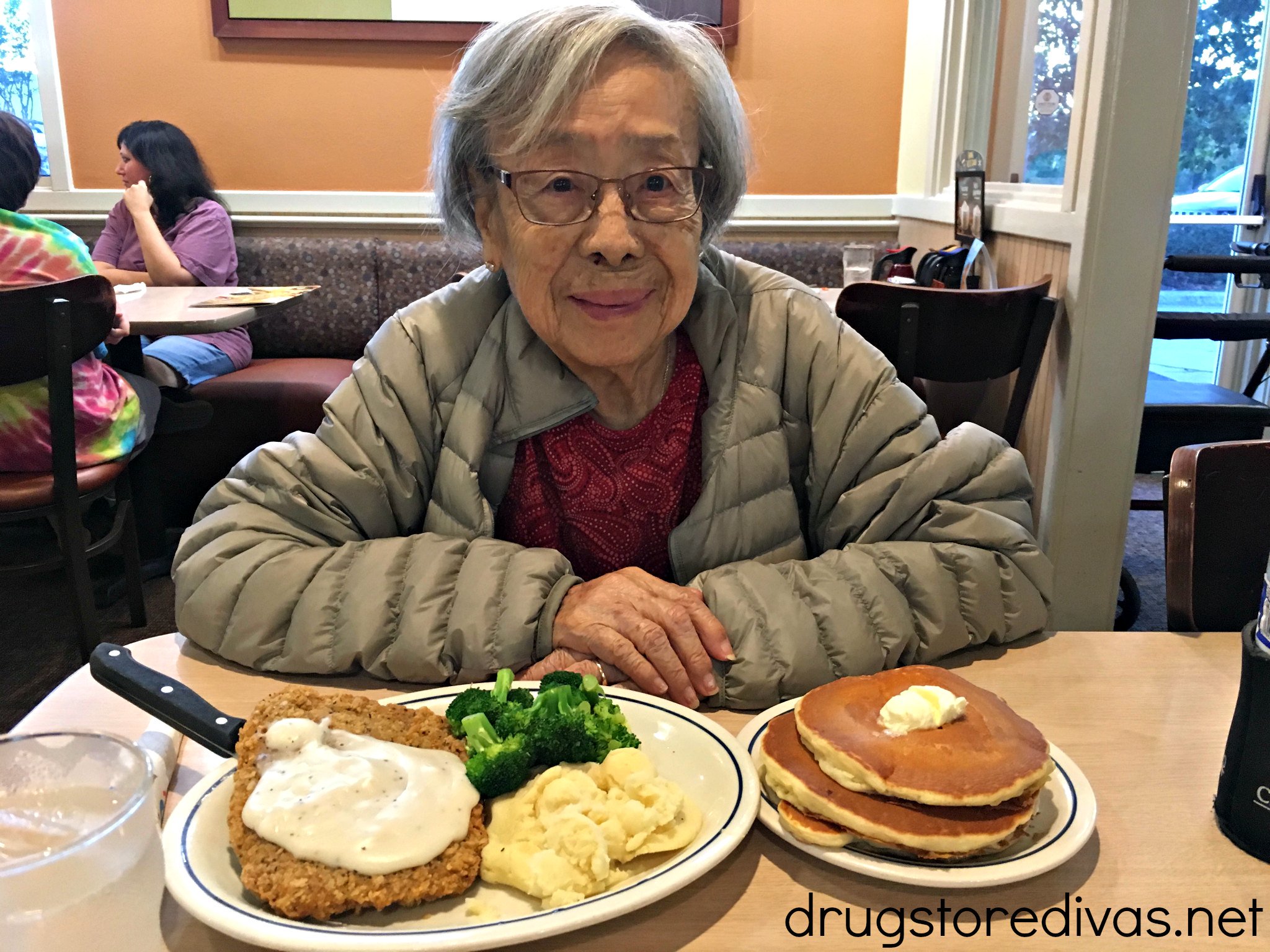 A woman at an IHOP with pancakes and other food in front of her.