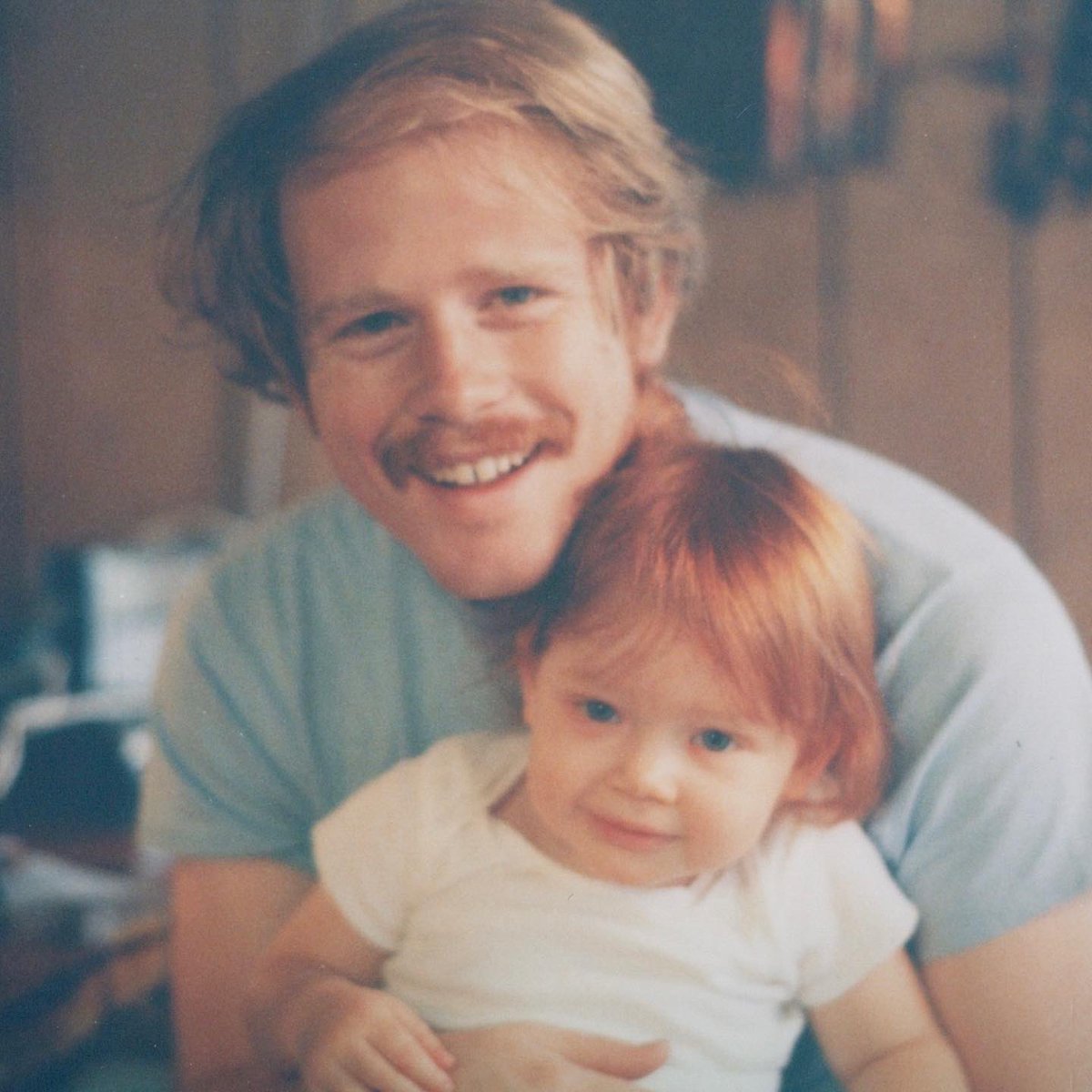 1983 Daddio holds an almost 2-year-old BDH in his arms as she rests on his lap. Ron wears a light blue t-shirt, bringing out both his and BDH’s matching eye color.