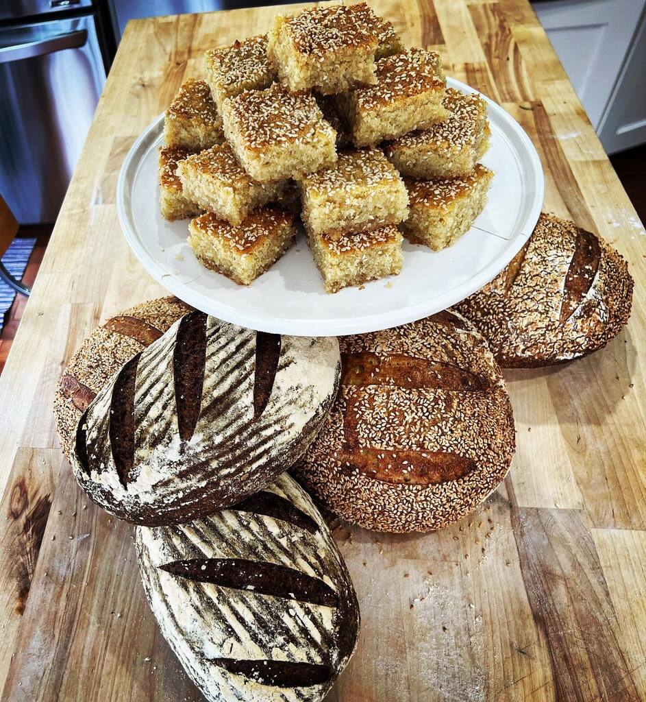 TITLE: Grey Day Doing Admin at Home

Still life, using flour. 

[sesame-semolina sourdough, cornmeal-molasses rye, and cinnamon namoura]

#baking #sourdough #pastrychef #lebanesefood instagr.am/p/CpTBKFoPpwT/