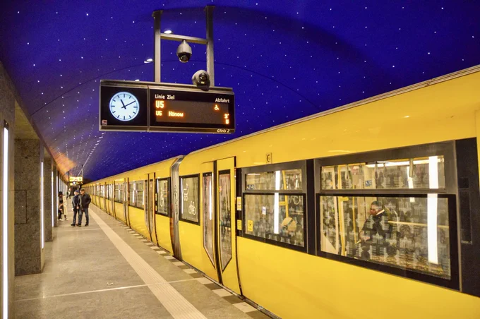 A bright yellow U-Bahn passenger train waits at the platform with doors closed at a station in Berlin.