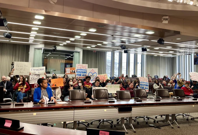Photo taken from Kristin’s seat of the audience in the hearing room filled with community members holding up signs in support of the HOME Act