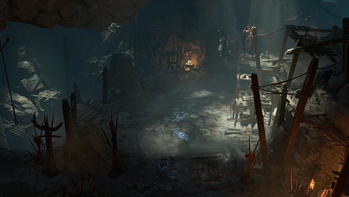 A screenshot of a Diablo 4 dungeon. It's a cave-like space, with sunlight beaming in from above, illuminating horrific decorations and decaying scaffolding in the shadows.