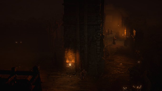 A screenshot of a Diablo 4 dungeon. Torches light an ominous, stone hallway, with hooded figures creeping out from the long shadows in the distance. 