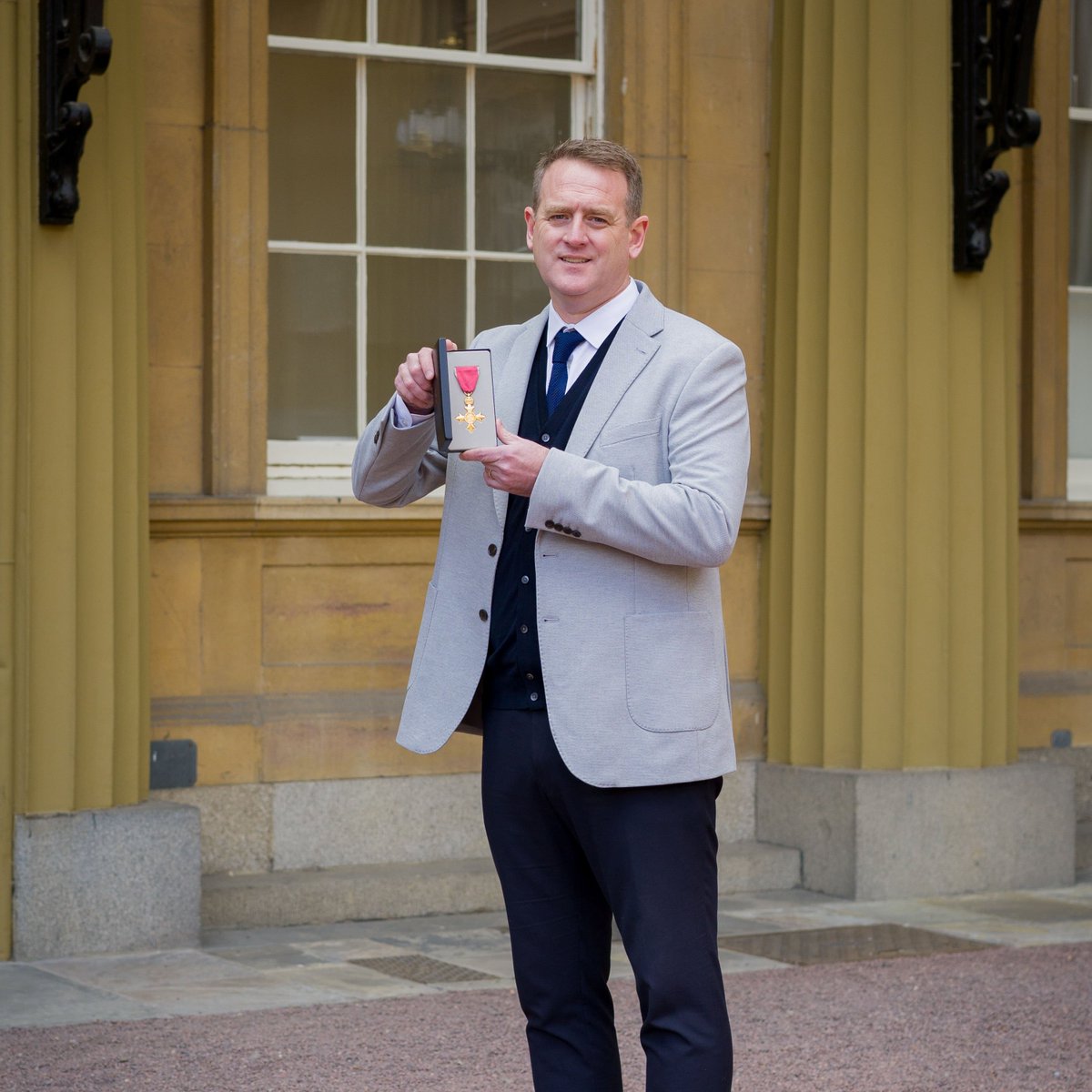 Ian Thornton holds his OBE outside Buckingham Palace.