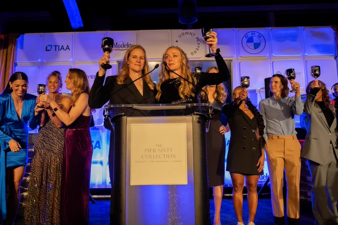 US Soccer President Cindy Barlow Cone and USWNTPA  President Becky Sauerbrunn toast to Equal Pay on stage with members of the USWNT Players CBA Committees behind them