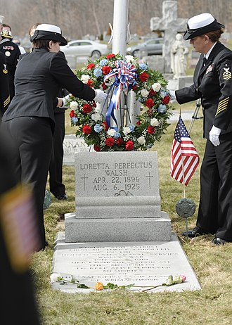 Two female Navy officers laying wreath on grave site of Loretta Perfectus Walsh in St. Patrick’s Cemetery, Olyphant, PA. 