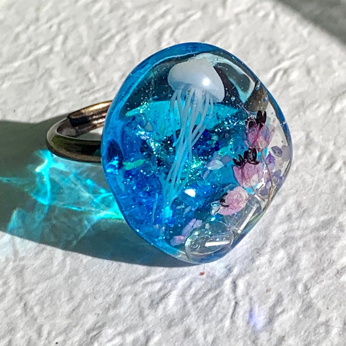BlueOnBlueSky's tweet photo. 立体的なクラゲを入れて、ドライフラワーやラメ、ビーズで水中にただようクラゲを閉じ込めたようなリングです。

透明感のあるブルーが綺麗です。

新作でーす。

https://t.co/w4w6hNJ2gV

#minne #minneで販売中 https://t.co/siRBXY6b6m