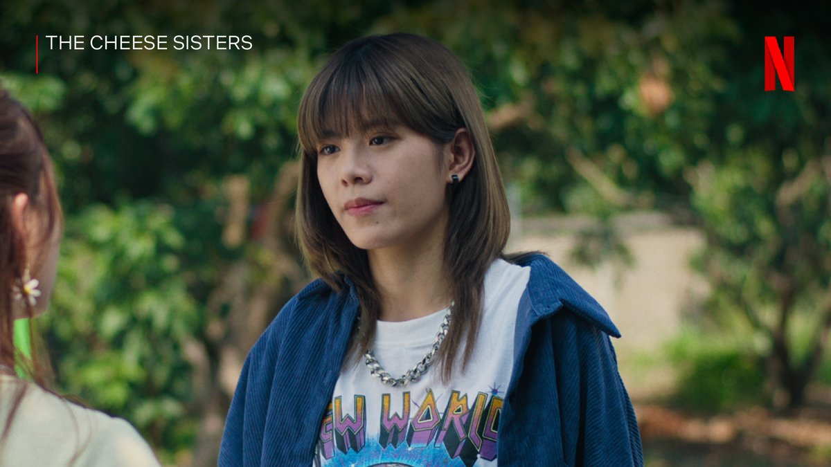 The image shows a young woman with bangs wearing a graphic t-shirt and a chain necklace, with "THE CHEESE SISTERS" text in the upper left and the Netflix "N" logo in the upper right, set against a green outdoor backdrop. The caption hints at a "straight uke" anime reference, which plays on the yaoi/BL genre term "uke" (typically the more passive/receptive partner), jokingly extending it to imply the character or show embodies that trope.