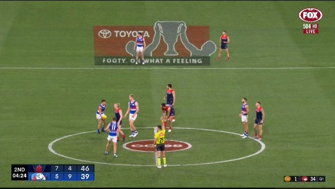 Melbourne v Western Bulldogs at the MCG. Before centre bounce, an ad for Toyota is projected on to the grass. It is actually a premiership cup being held by two men, but it kind of looks like a uterus 