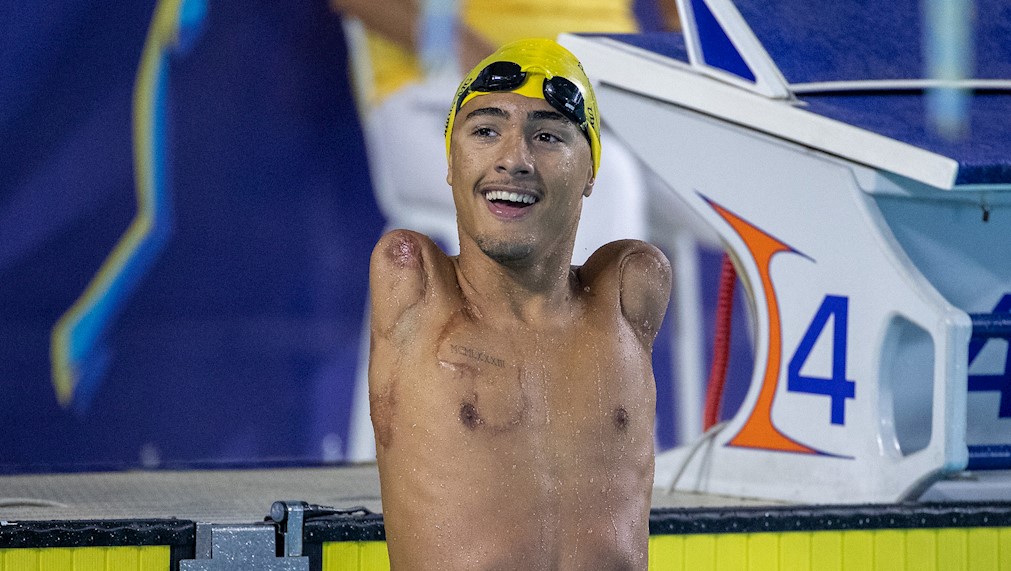 Foto do atleta Samuel Oliveira na piscina pós competição. Ele usa touca amarela e óculos preto. Ele está sorrindo para a foto.
