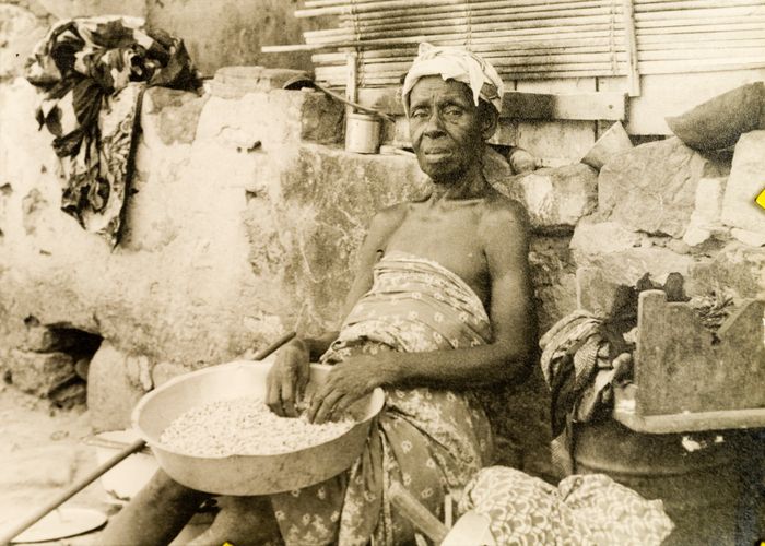 OwulaJB's tweet photo. An elderly Ga woman sits against a roadside wall, selling nuts or grains from a bowl, Accra, Gold Coast (now Ghana), 1951 https://t.co/gRq0DD6b8h