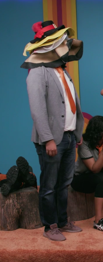 a cropped screenshot from dropout's "game changer." tao yang is standing straight with his arms at his sides. his entire face, head, and neck are obscured by the stack of 5+ sunhats of varying sizes and colors that he is wearing