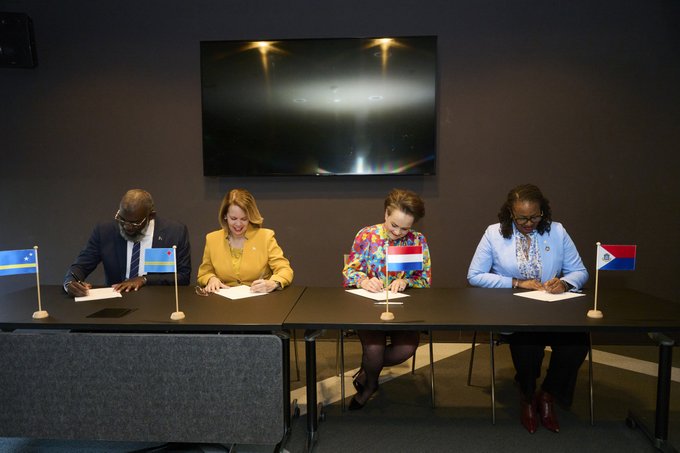 vlnr: minister-president van Curaçao Pisas, minister-president van Aruba Wever-Croes, Alexandra van Huffelen en minister-president van Sint Jacobs houden tekenen papieren. Voor hen de vlaggen van de landen.