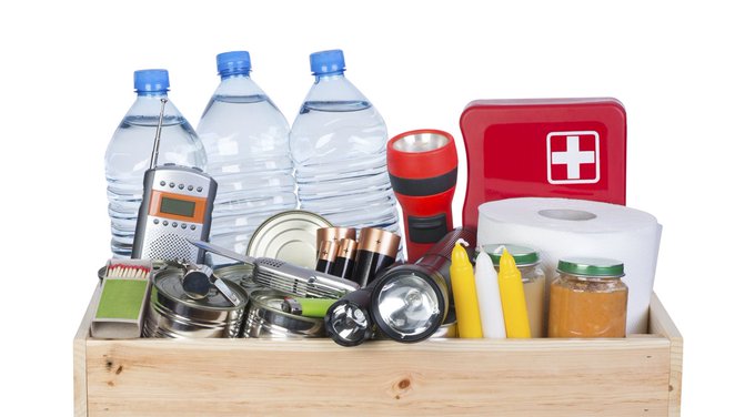 Photo of a emergency kit: Water bottles, flashlight, candles, toilet paper, batteries and a first aid kit.