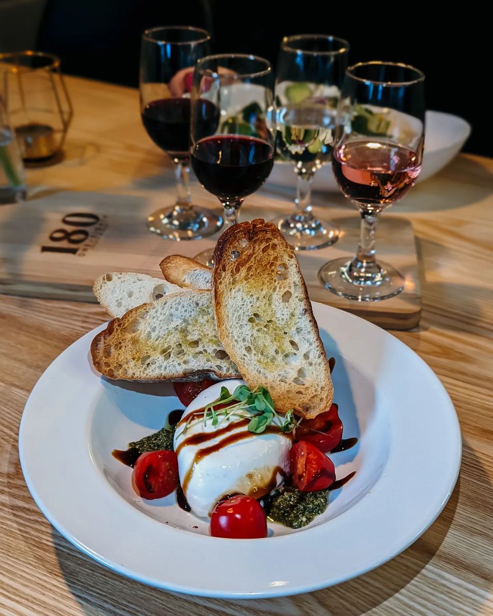 It's #FoodieFriday! Are you looking for a match made in heaven? ✨ Check out this Italian Burrata cheese served with pesto, cherry tomatoes, balsamic glaze, and crostini from <a href="/180wines/">180 Estate Winery</a>. Pair it with a personalized wine flight and you’re in for a fantastic Friday night.🍷