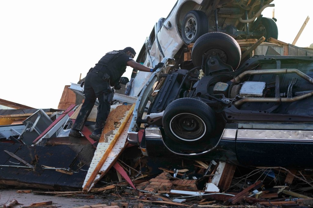 A sheriff's deputy climbs onto a pile of wind-tossed vehicles to search for survivors or the deceased at Chuck's Dairy Bar in Rolling Fork, Miss., Saturday, March 25, 2023. Emergency officials in Mississippi say several people have been killed by tornadoes that tore through the state on Friday night, destroying buildings and knocking out power as severe weather produced hail the size of golf balls moved through several southern states. (AP Photo/Rogelio V. Solis)