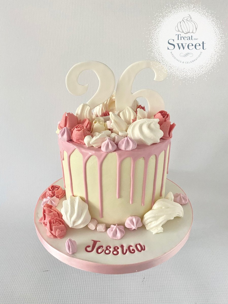 Chocolate layer cake coated in buttercream with pink chocolate drip. Topped with meringue, marshmallows and buttercream flowers