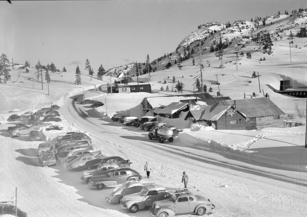 The "Ski-Hi" at Donner Summit looks busy this winter day c. 1949. The sign on the building closest offers "Ski Hi Dancing," while the sign over the entrance offers "Fine Food." Just to the upper right of the photo, we can see the snow sheds of the railroad entering the Summit