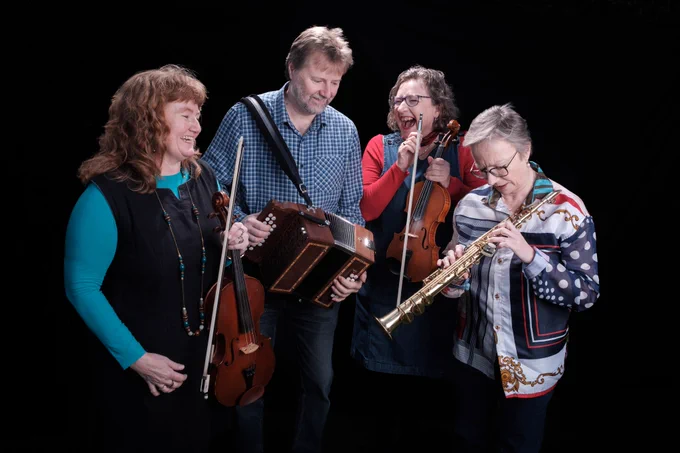 Narthen holding their instruments and laughing and joking together. Sarah Matthews has a viola, Doug Eunson a diatonic accordion, Fi Fraser a fiddle and Jo Freya a soprano saxophone.