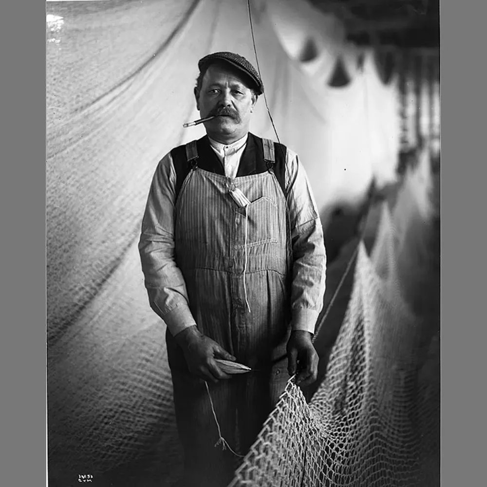 An Alaskan fisherman, taking a quick break from hanging his net. He's got a shuttle in one hand, another one in his overalls pocket, and a smoke in his cigarette holder. Photo by the famous Asahel Curtis, 1916. 🐟