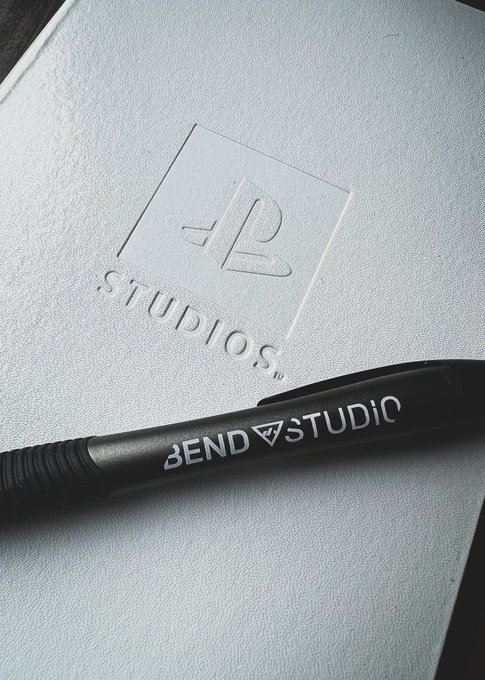 A black and gray pen with a white Bend Studio logo on it sits on top of a white notepad with the PlayStation Studios logo engraved on the cover.