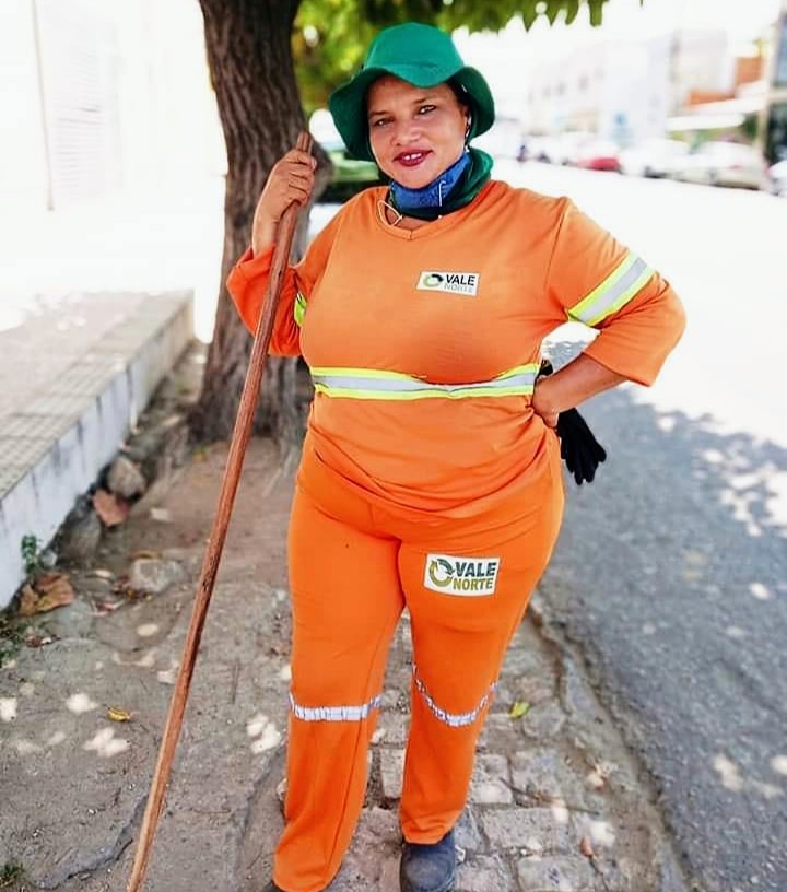 Kathgurgel's tweet photo. Hoje eu conheci Adriana. Adriana é gari aqui na cidade de Mossoró, no RN. 
Hoje, pra sorte minha, ela estava varrendo o meio-fio, perto de onde estacionei.
“– Tem sabor de mel, tem sabor de mel, a minha vitória hoje tem sabor de mel..." - Enquanto me aproximava, a voz ia ficando ainda mais empolgada.
– Oi, tudo bem? Menina, que coisa boa vê-la trabalhando cantando com tanto entusiasmo assim logo cedo! Ganhei meu dia! – disse, me aproximando daquela mulher iluminada, com um batom vermelho nos lábios, um lápis preto, realçando seus olhos verdes, e o rosto bem protegido por uma maquiagem.
– Só trabalho assim, mulher, da hora que chego até a hora que eu vou embora. Se não tiver a música nos meus ouvidos, fico aperreada – respondeu, já tirando um dos fones de ouvido, encostando a vassoura numa árvore, para me dar atenção.
Ela tinha um sorriso tão escancaradamente verdadeiro que tomava o seu rosto todo! 
– Faz tempo que observo você trabalhando nas ruas, sempre animada, feliz. Que bom que hoje deu pra conversar com você. Qual seu nome?  
– Meu nome é Adriana. Trabalho por essa área mesmo. Das sete à uma hora da tarde, tô limpando tudo por aqui e cantando. 
– Adriana, muito prazer, meu nome é Katharina e trabalho aqui ó, bem pertinho – falei, apontando para o prédio onde trabalho. – Há quanto tempo que você está na profissão de gari?
– Vixe, mais de dez anos... Não é não, seu Manoel? – perguntou a um outro colega de trabalho, um senhor que varria a outra esquina. Seu Manoel concordou com a cabeça e deu um sorriso discreto.
– Adriana, e sempre você trabalha assim, alegre, animada?
– Minha filha, acordo às 3h30, 4h, ajeito tudo em casa e já começo a me preparar para vir trabalhar. Eu amo ser gari! Tem gente que não gosta muito não, sabe? Tem vergonha. Deus me livre ter vergonha de ser gari, eu tenho é muito orgulho! Quando você 
vê uns garis com o chapéu bem arreado pra frente, ou um lenço bem aqui, ó, cobrindo a boca e o nariz, é porque não quer mostrar pro povo que é gari. Diga aí do absurdo?! – ela contava indignada.
– Sério?
– Sério, minha filha, gente que trabalha de mau humor, todo abusado. Eu não, coloco a minha maquiagem, o meu protetor, pego as minhas músicas e quero mesmo é chegar logo aqui.
– E o que você mais gosta de ouvir? 
– Mulher, eu ouço de tudo. Sertanejo, romântico...Agora, só não ouço rock. Rock me dá uma agonia no juízo – falou, dando uma gargalhada. 
– Aí você passa as músicas para o seu celular?
– Não, minha filha mais velha, Ingrid.
– Quantos anos ela tem? Você tem outros filhos?
– Tenho sim. Tem Ingrid, com quinze anos, Vitória com onze e Marco Antônio com seis. Todos criados com esse meu emprego maravilhoso! 
Ela tinha mesmo muito orgulho do seu ofício. 
– Meu marido, Antônio Carlos, já sabe que todo mundo me conhece. Tem gente que até para, pra tirar foto comigo! – conta, soltando mais uma gargalhada.
– Adriana, tão bom conhecê-la! Uma mulher feliz. Fico feliz também! 
– Pois é, Katharina, a gente não tem do que reclamar não, mulher! Se a gente tiver com saúde, tá tudo bem! – falou olhando para mim, com uma mão segurando o cabo da vassoura e a outra no meu ombro.
– Adriana, de vez em quando eu gosto de escrever sobre alguns encontros felizes da minha vida, aí publico nas minhas redes sociais. Você se incomodaria se eu escrevesse sobre a sua história e publicasse, junto com uma foto sua?
– Mas mulher, claro que não, eu vou é gostar! Agora, você tem que me marcar no instagram para o povo ficar sabendo quem eu sou. Peraí, vou olhar aqui qual é mesmo o meu instagram. – Foi olhar no celular. – Pronto, anote aí: adrianamontedasilva, tudo junto. 
 – Ótimo, vou fazer o texto e marcá-la.
– Pronto, quero ver mesmo. Agora, mulher, tire uma foto bem bonita, e cuidado para o sol não ficar muito no meu rosto, para eu não sair de olho fechado no retrato. 
Hoje eu conheci Adriana. Uma iluminada gari que me passou as melhores lições sobre trabalho, paixão, ofício, entusiasmo e gratidão. 

(Crônica publicada em 2019)