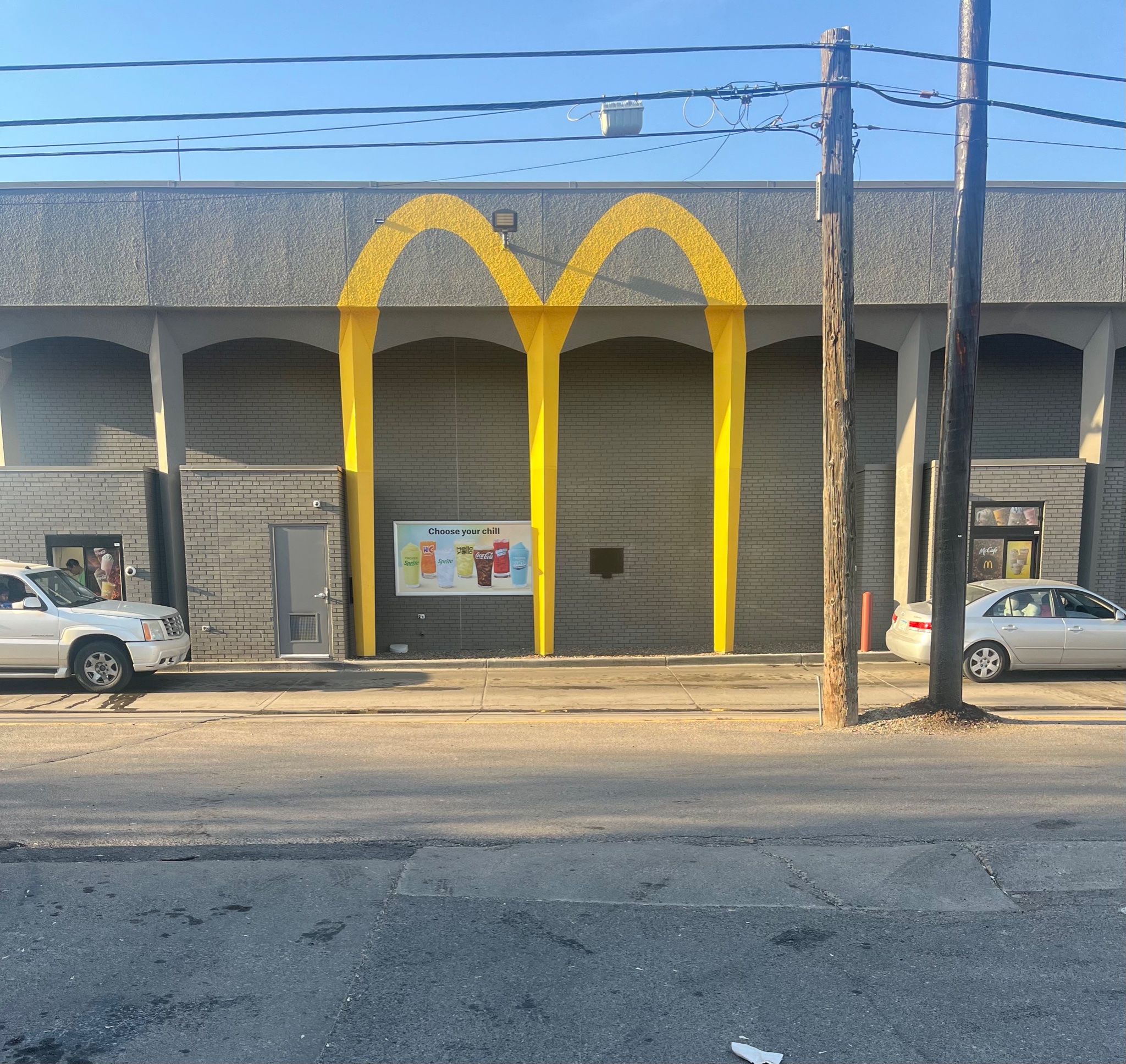Arches painted on side of two-story former bank with utility poles and raking light and cars at each service window