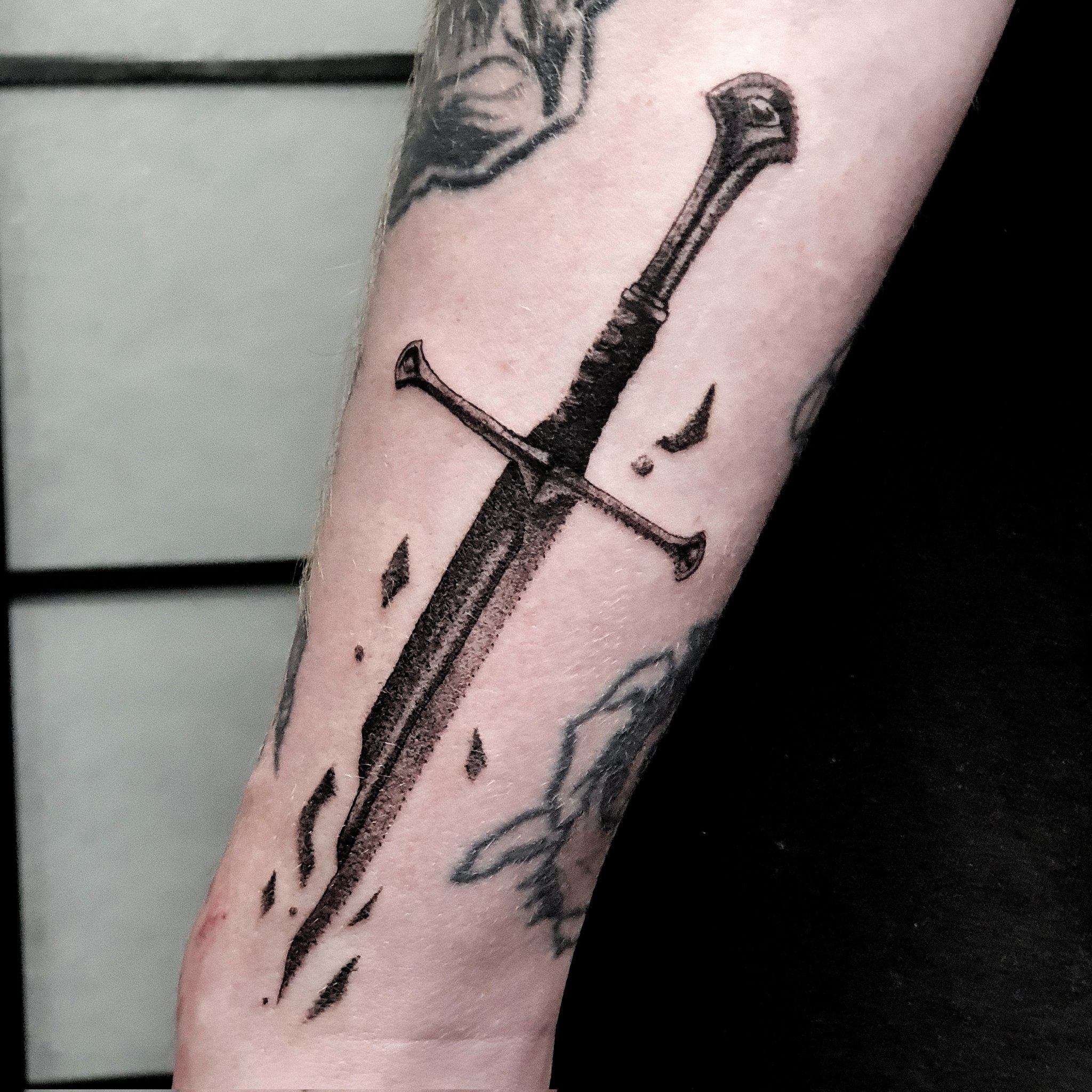 Fine line broken sword tattoo on the inner forearm.