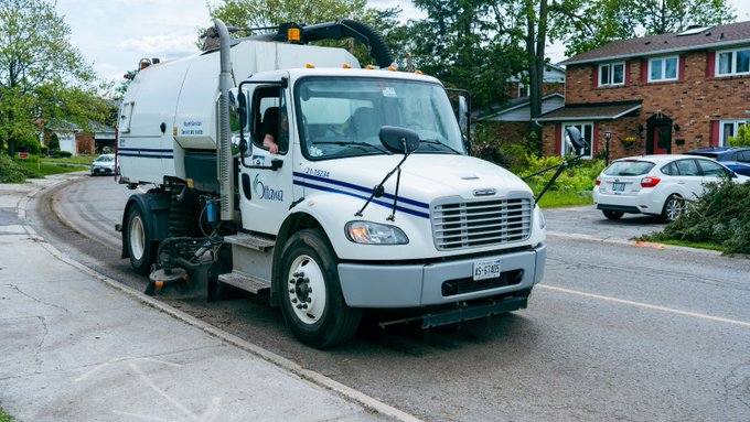 A City of Ottawa street sweeper truck is cleaning up debris on a residential street. 