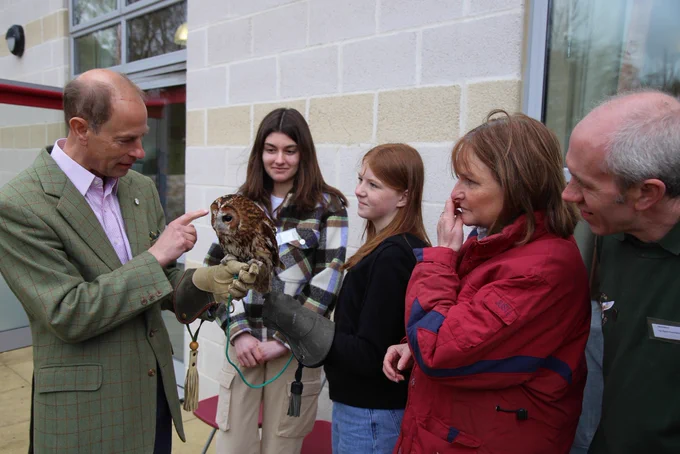 The Duke, holding an owl whilst standing with young people outside at a DofE Open Award Centre.