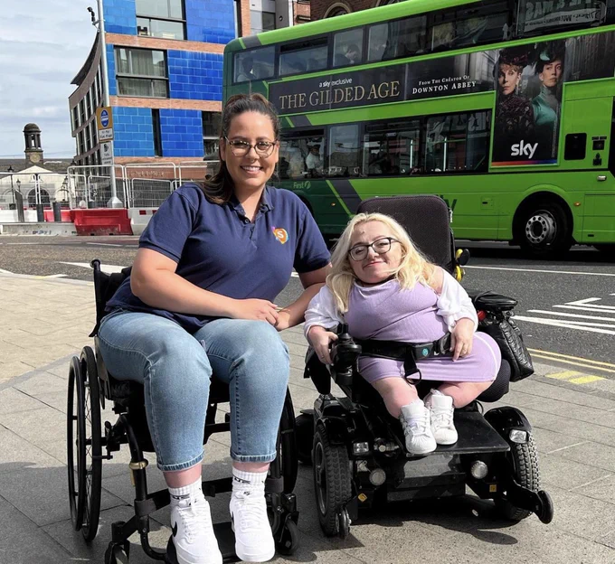 Jennie and gem in their wheelchairs smiling on street pavement