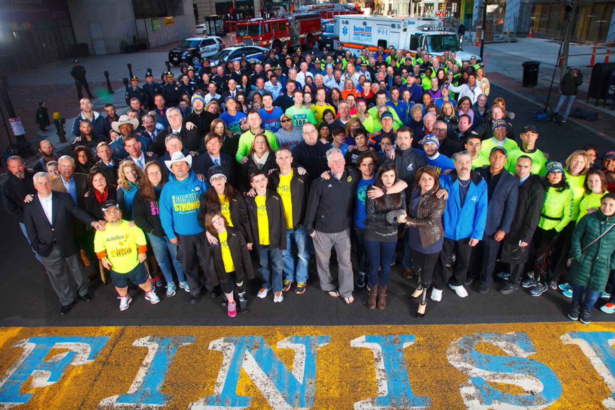 A photo of survivors, families, elected officials, law enforcement members, and first responders at the Boston Marathon finish line.
