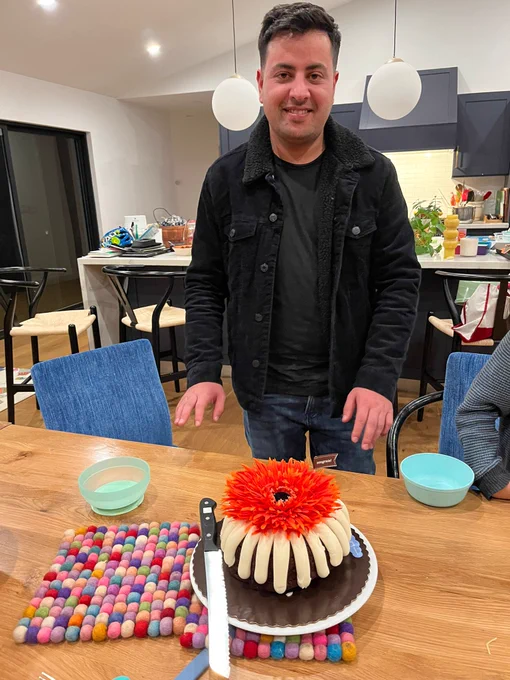 Ali stands in front of a kitchen table, with a chocolate bundt cake with a flower on top.