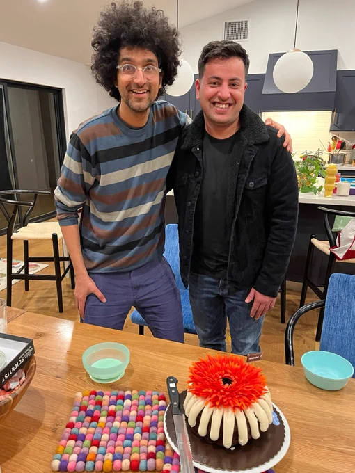 Latif and Ali stand in front of a kitchen table with a chocolate bundt cake and a flower on top.