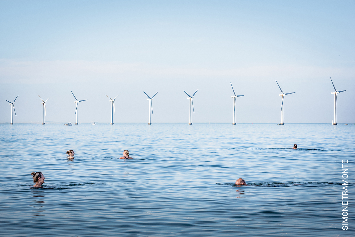 Photo of the Day | People swim at Amager Strand, Denmark, near a wind farm which is co-owned by 8,552 electricity consumers, and serves more than 40,000 Copenhagen households, 13 July 2021. By <a href="/SimoneTramonte/">Simone Tramonte</a>, awarded in the #WPPh2023 Contest: bit.ly/3Avut0t