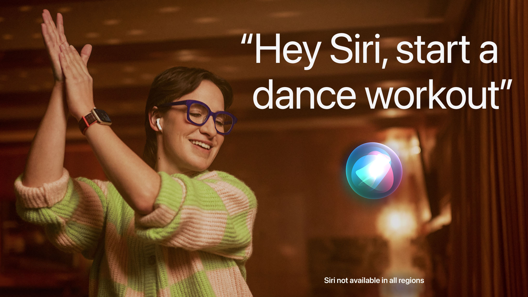 To start a dance workout say, “Hey Siri, start a dance workout.” Siri is not available in all regions. A person is shown wearing AirPods and their Apple Watch while dancing around their living room.