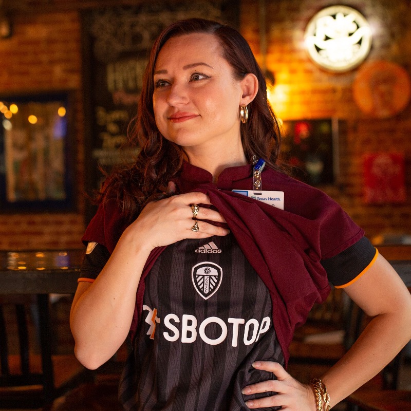 PLinUSA's tweet photo. Wearing your club's kit under your work clothes to demonstrate your passion? That's a tradition we can get behind 👕

Meet @beckycllns88, a @LUFC fan and pharmacist in Fort Worth, Texas, who turned tweets about her favorite @ussoccer players into #PL fandom.

#PLFansofAmerica