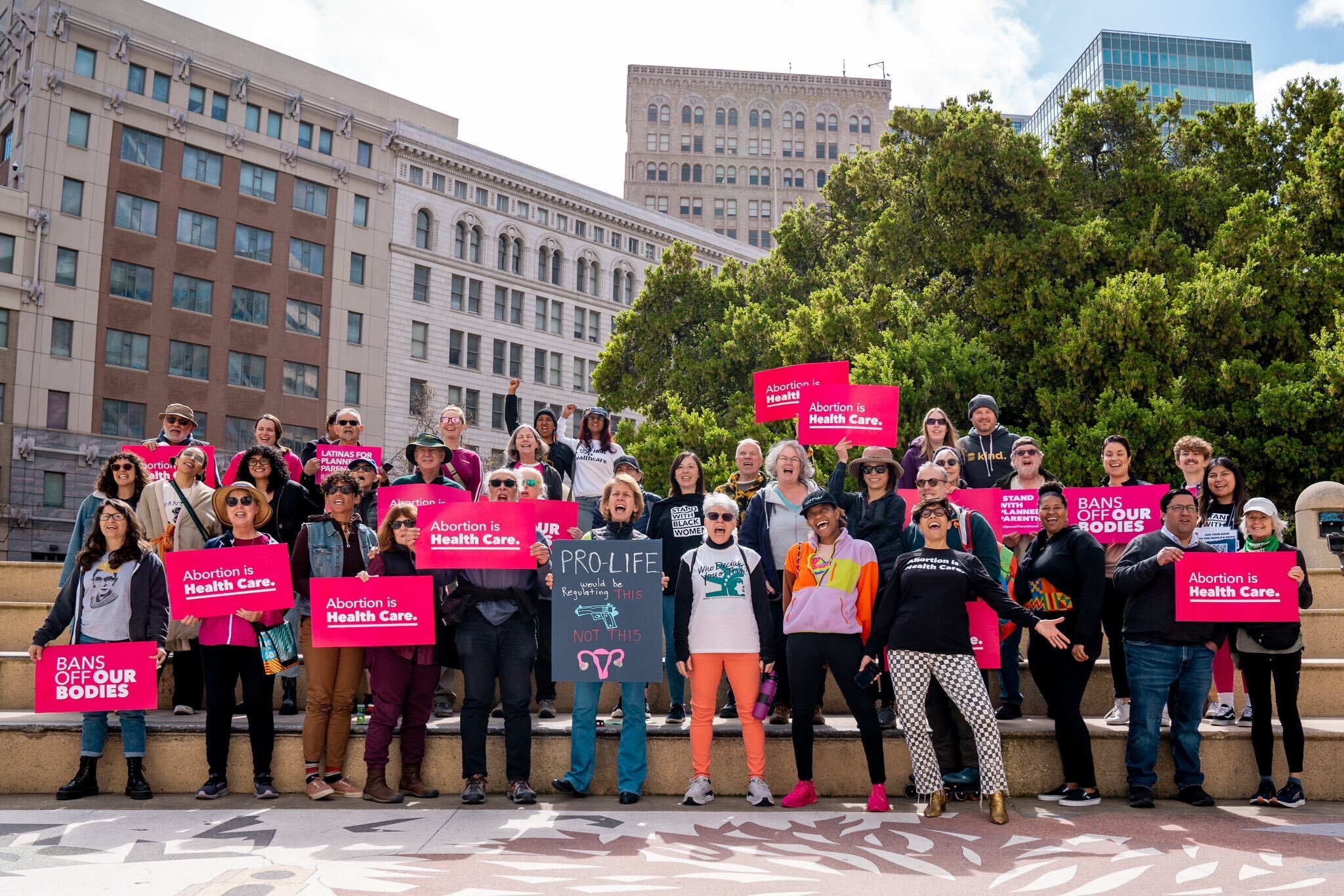 A group photo of activists from planned parenthood and supporters  in Oakland, CA, holding pink signs that say "abortion is health care”