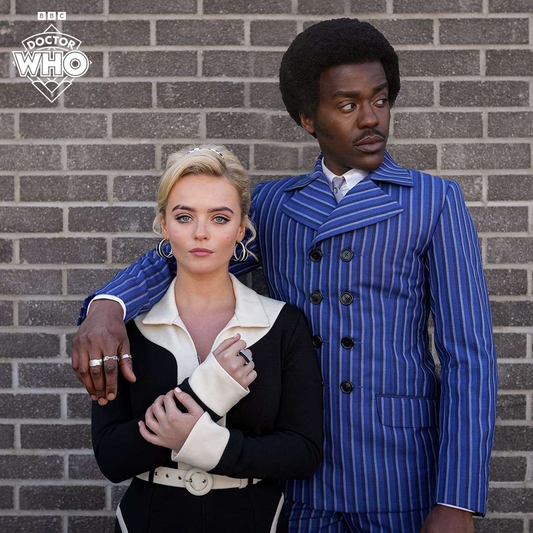 Ncuti Gatwa and Millie Gibson as the Doctor and Ruby Sunday, dressed in 1960s-style clothing, posing in front of a brick wall.