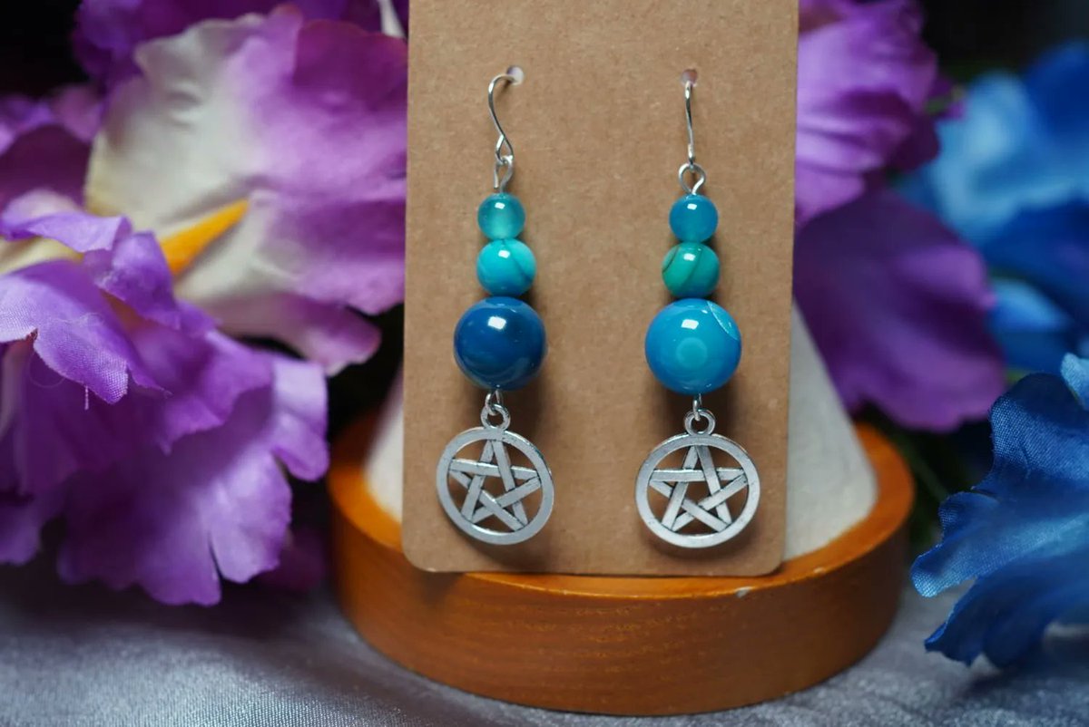 Bring the soothing energy of the ocean with our blue agate and shell earrings featuring pentacle charms! Blue agate is known to promote calmness, inner stability, and communication skills.  🐚✨ #metaphysicaljewelry #blueagateearrings #pentaclecharm  buff.ly/3MuBeXF