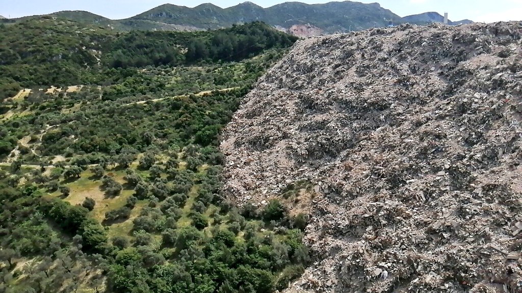 Hatay Narlıca'da molozların döküldü alanın son hali. Zeytin ağaçları moloz yığınlarının altında kaybolmuş. Daha düne kadar su içilen dere kaynağı kesildiği için kurumuş. Yaşam ve ölüm arasındaki çizgi gibi beton can almaya devam ediyor.