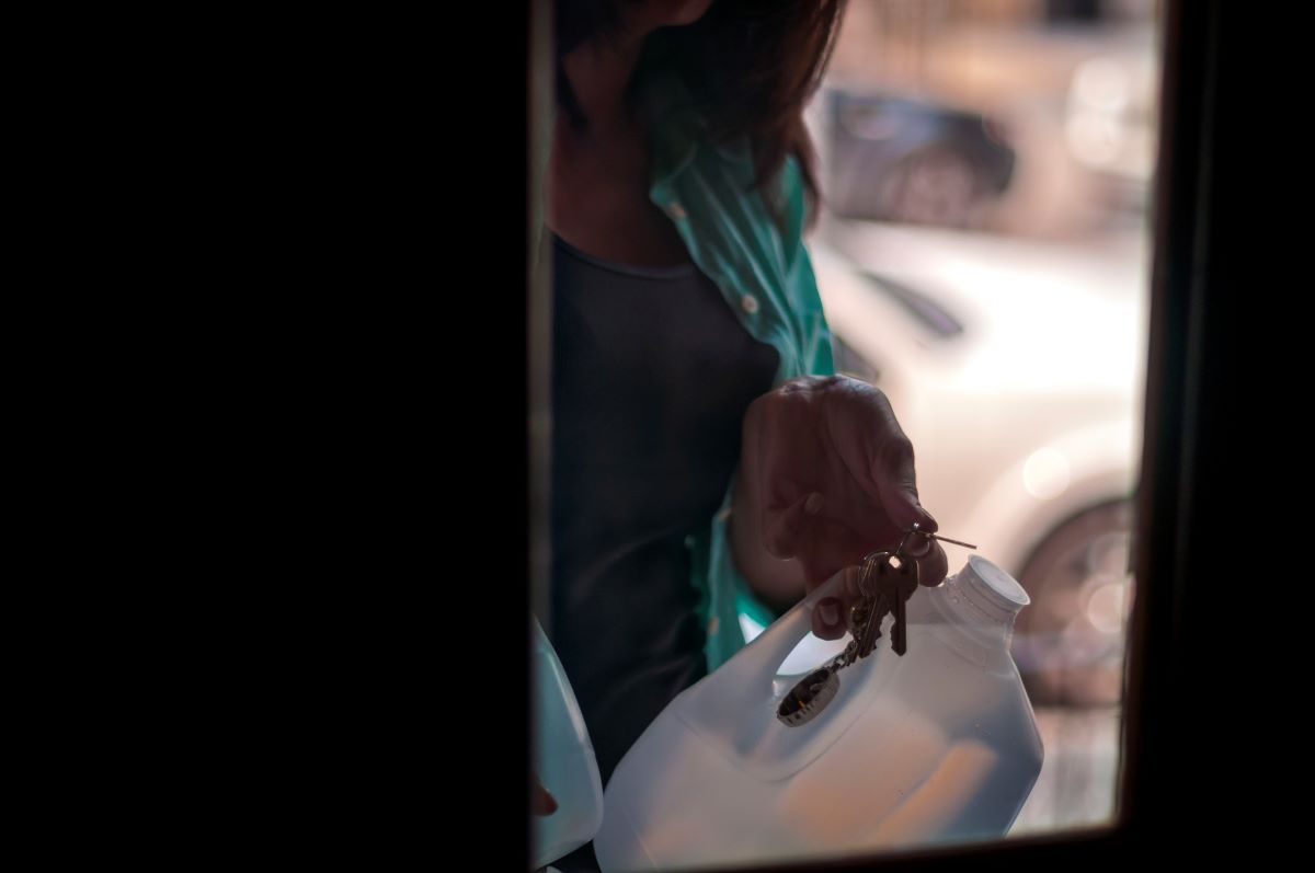 A person walking into a house with gallons jugs of water in their hands.