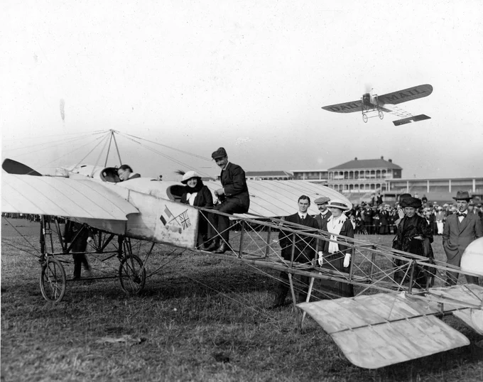 Black and white photograph of people sat on early monoplane