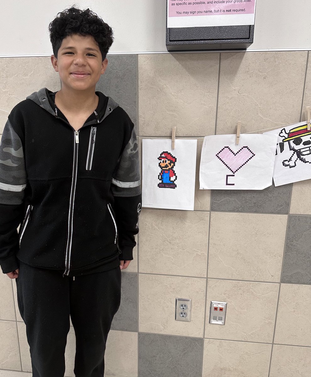 This week in #artclass: This student was so proud to have his #pixelart hanging outside our classroom, he asked me to take a picture for his mom 🥹! We won’t have to hang these on a rope for much longer because I have some of my own display cases on the way!