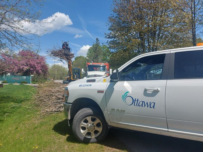 A photo of a City of Ottawa vehicle. In the background, a backhoe is picking up debris from a storm.