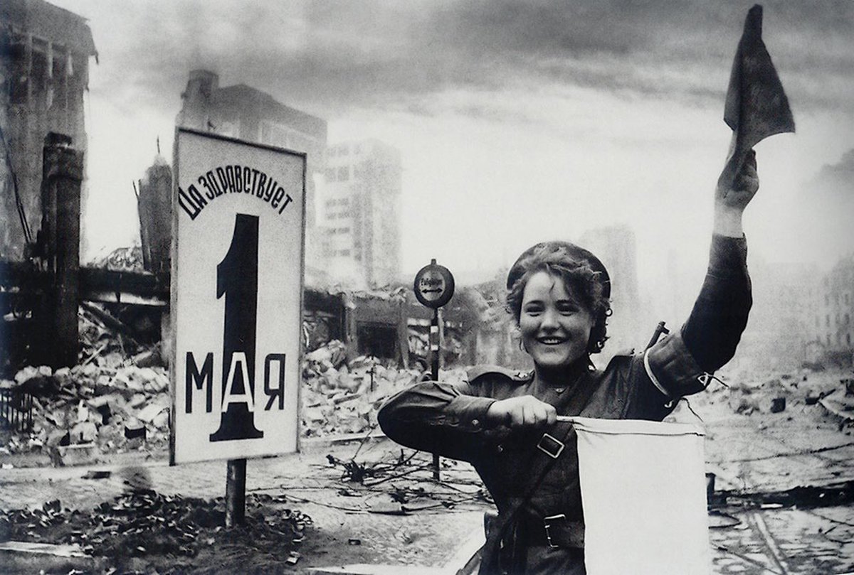 Russian Corporal Mariya Shalneva directs Red Army traffic through the ruined streets of Berlin, standing in front of Soviet sign celebrating 1 May.